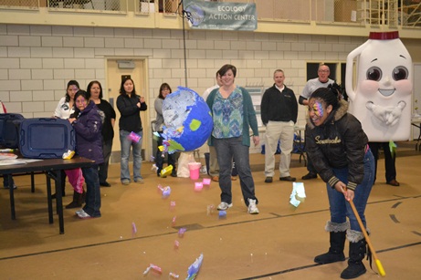 A girl holding a stick after hitting a earth-shaped piñata with EAC staff members watching at a recycling event.