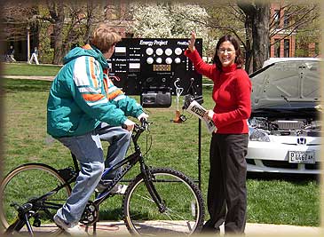 A man riding a bike past a woman presenting about the energy project.