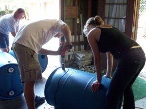 Three people constructing a rain barrel