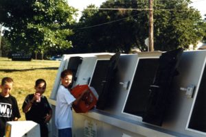 Three kids using Normal's recycling bins to recycle plastic and cans.