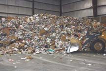 Truckloads of recyclable waste are dumped into a huge pile. Front-end loaders carry the waste to the beginning of the sorting process.