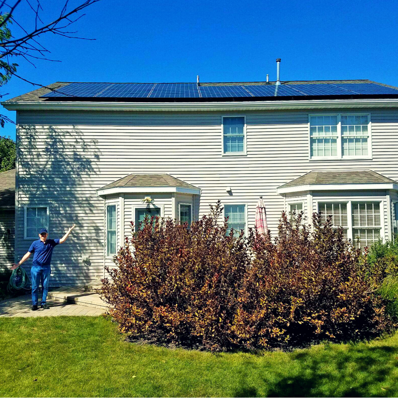 A resident standing in front of their home, arms outstretched showing off their solar panels 