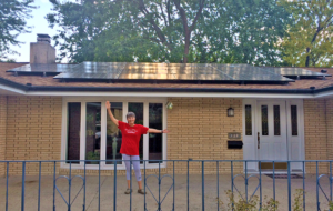 Man standing in front of a home with solar panels with his arms outstretched 