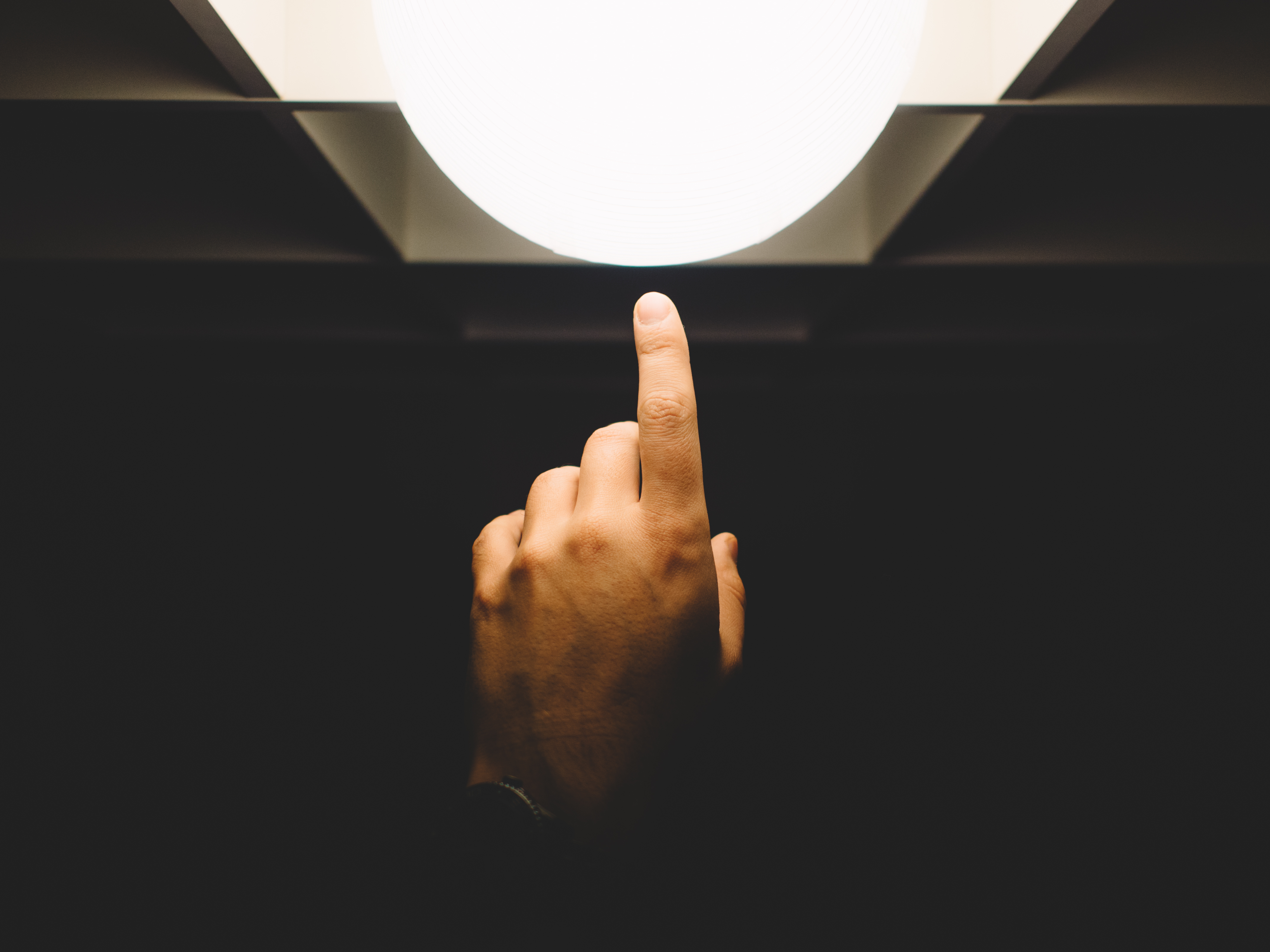 A hand pointing upwards toward a light against a dark background.