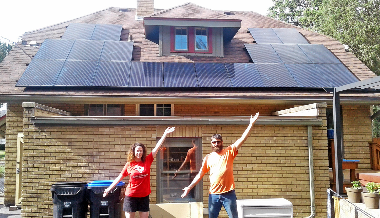 Two people standing in front of a house with newly-installed solar panels on the roof.