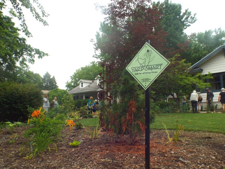 A garden with several people looking around it and a yellow yard smart sign with the yard smart logo.