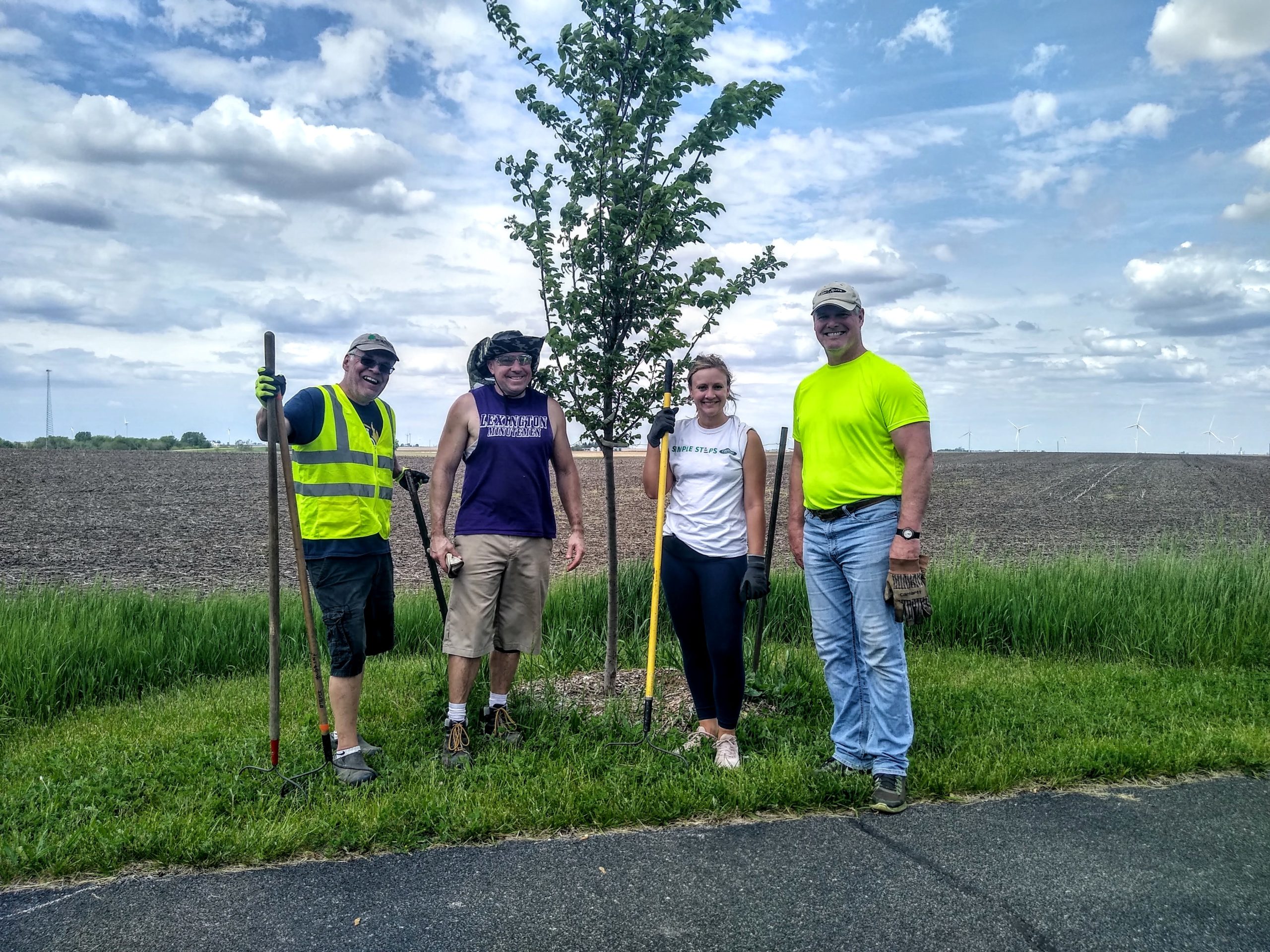 Four volunteers standing beside a tree they planted on the Route 66 trail