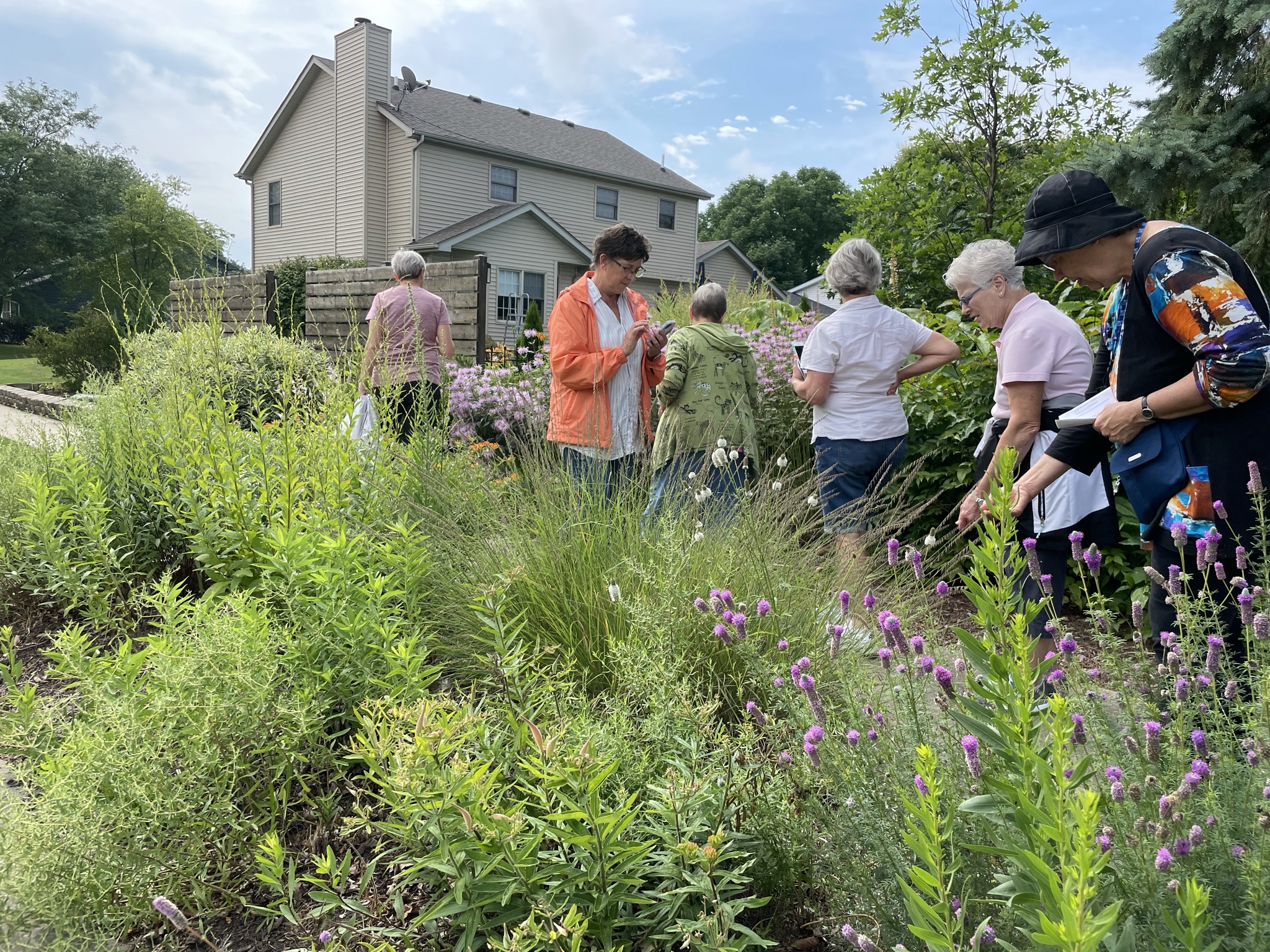 A group of people walking through a flower garden as part of the Yard Smart Garden Walk.