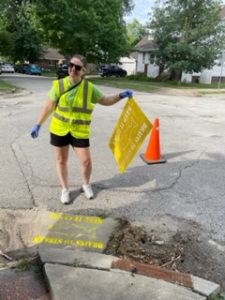 Woman holding a stencil which reads "Drains to Stream Keep Clean" after stenciling near a storm drain.